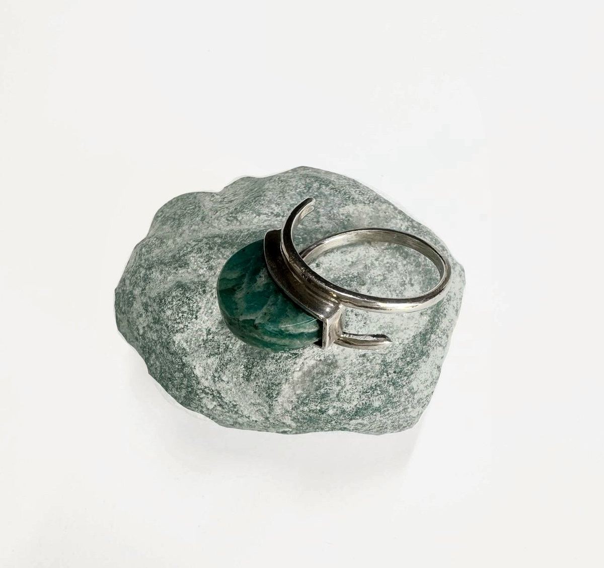 Anillo abierto de plata con una piedra verde azulada sobre una roca.