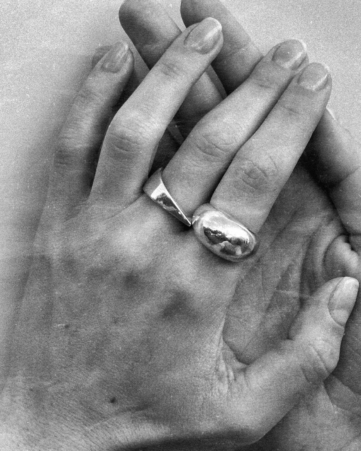 Black-and-white photograph of two hands wearing two domed silver rings, by AGAPE.