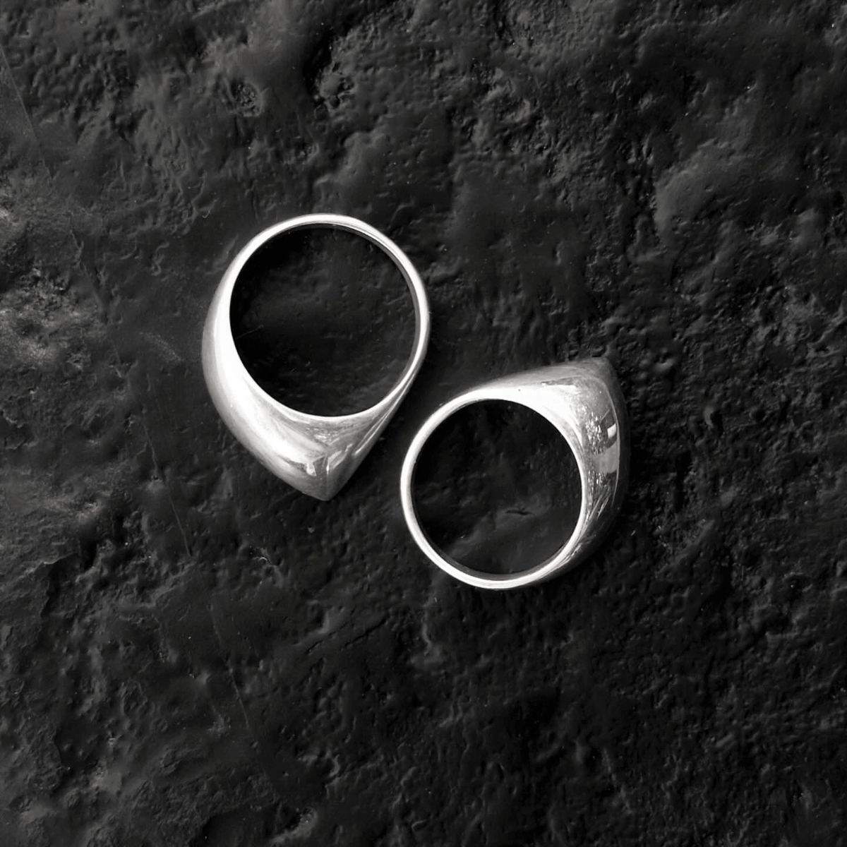 Two polished silver signet rings on a rough black surface.