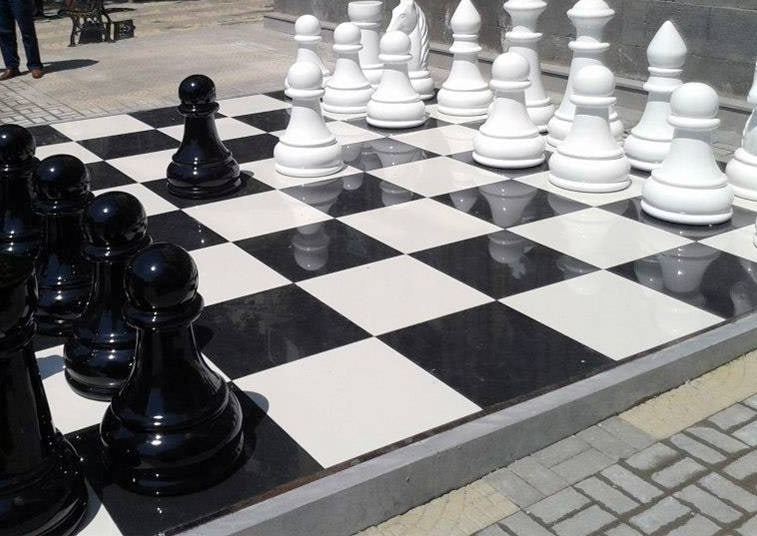 Black and white pieces of a giant fibreglass chess set on an outdoor board in Yerevan.
