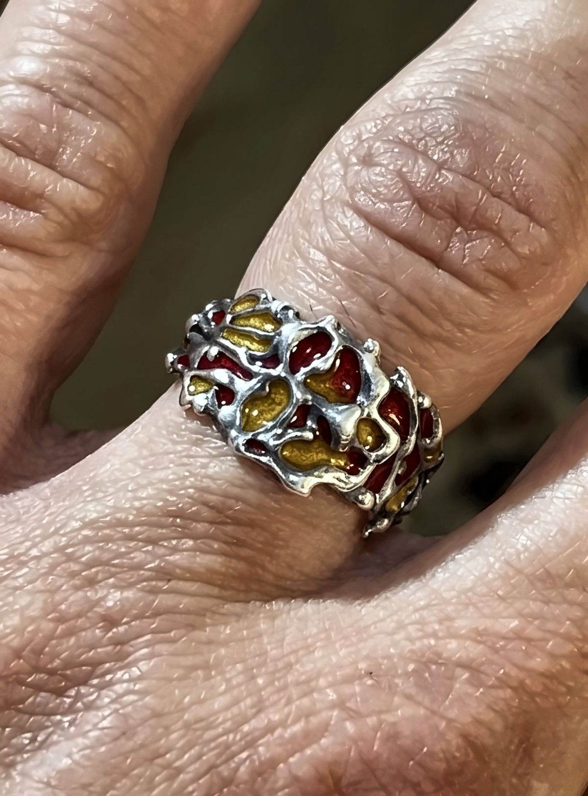 Silver ring with red and yellow enamel, worn on a finger.