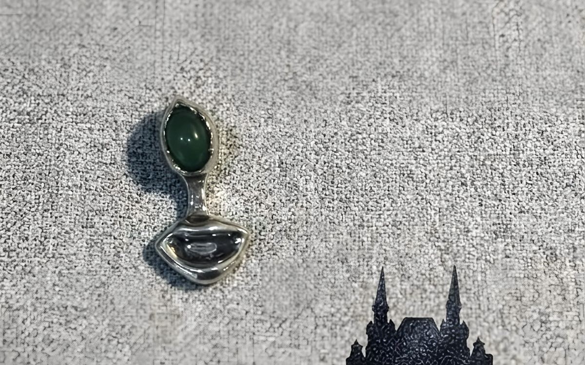 Silver lip-shaped pendant with a green nephrite, on grey cloth.