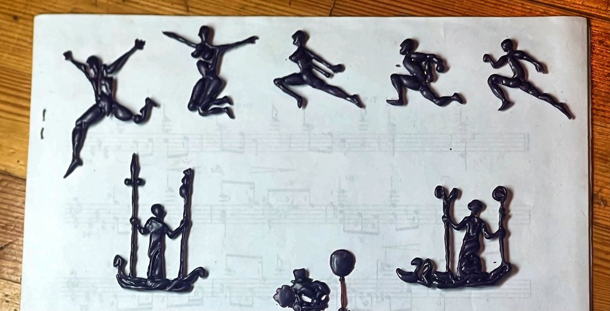 Dancer and warrior figures carved in wax by Momik, on sheet music.