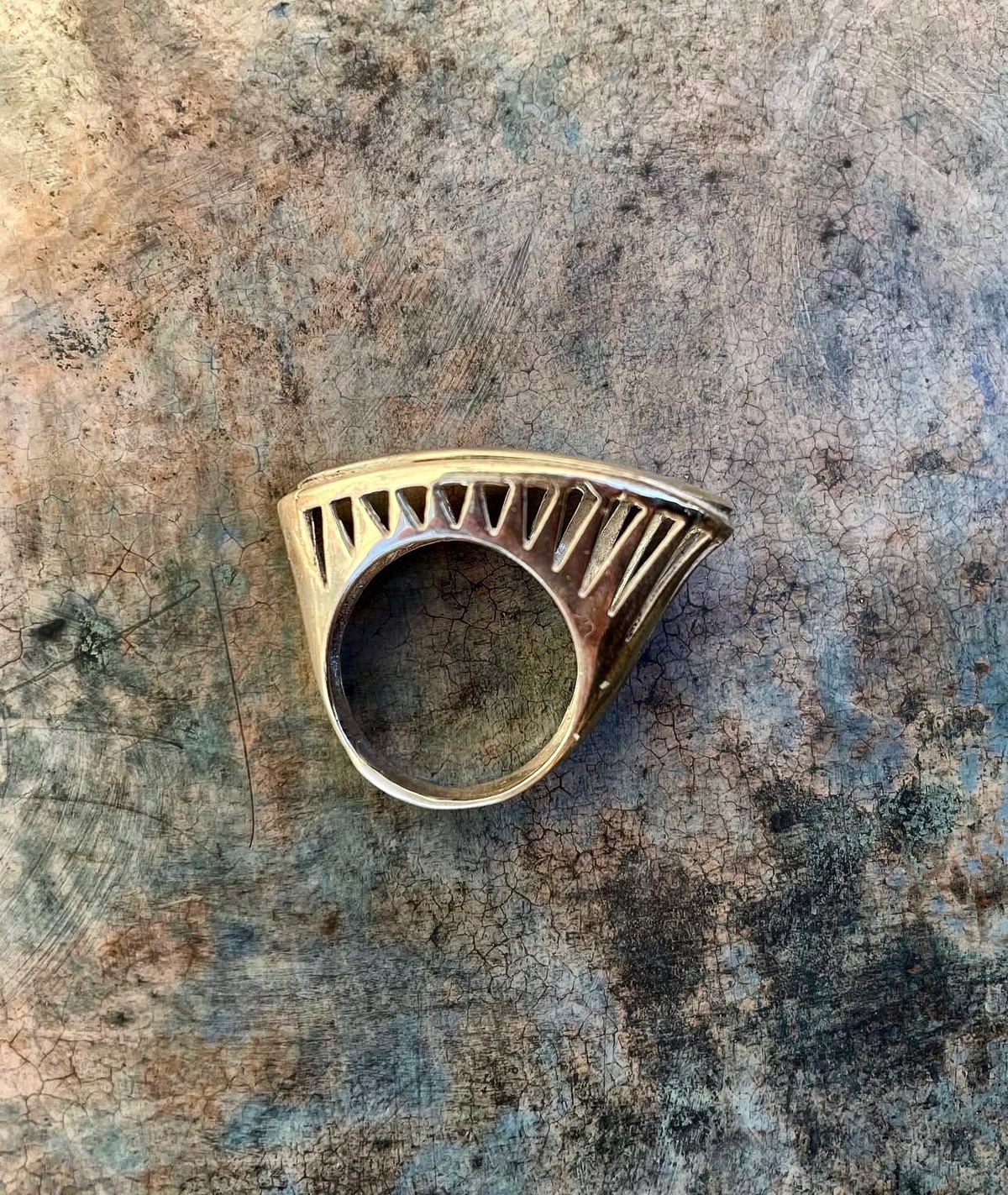 Anillo de plata calado en forma de abanico sobre fondo pintado.