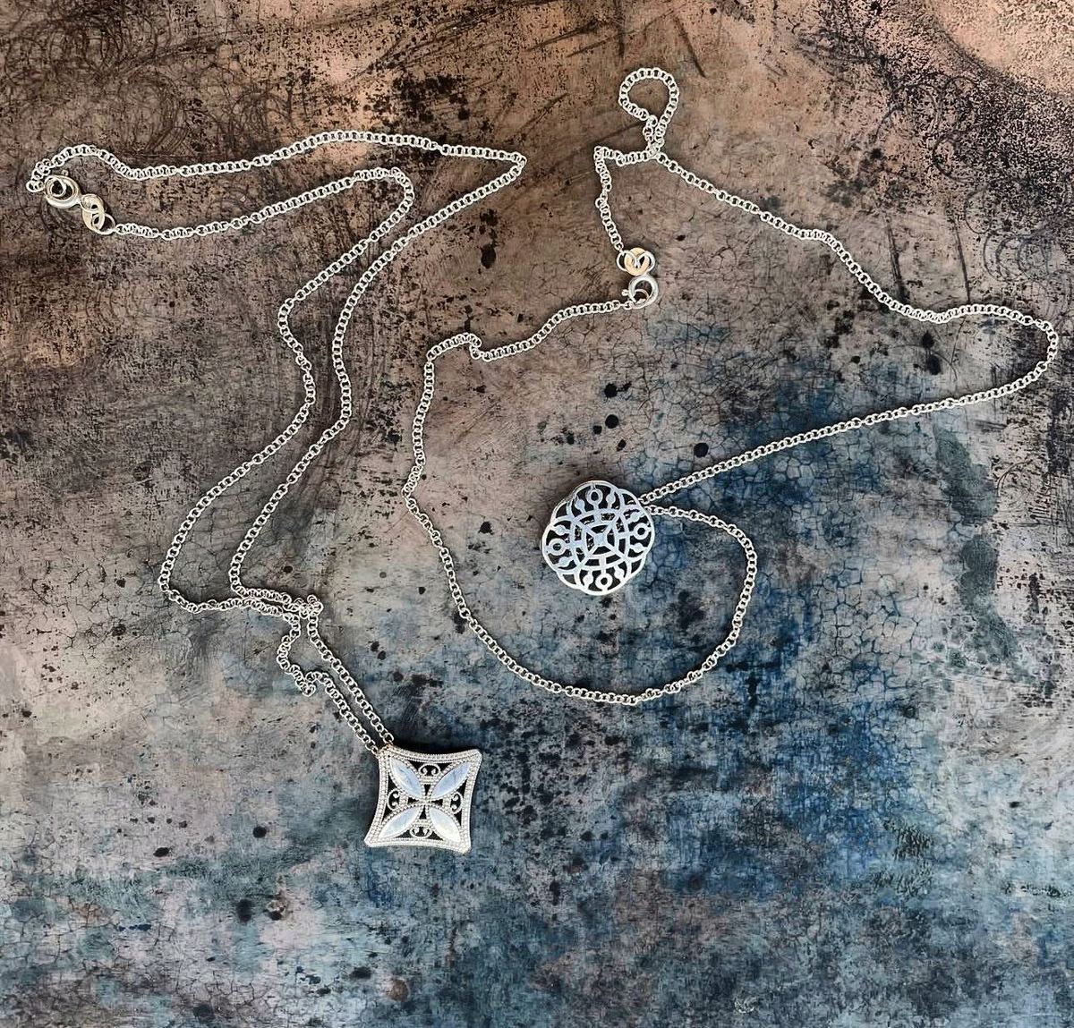 Dos colgantes de filigrana de plata sobre tabla pintada azul cobre.
