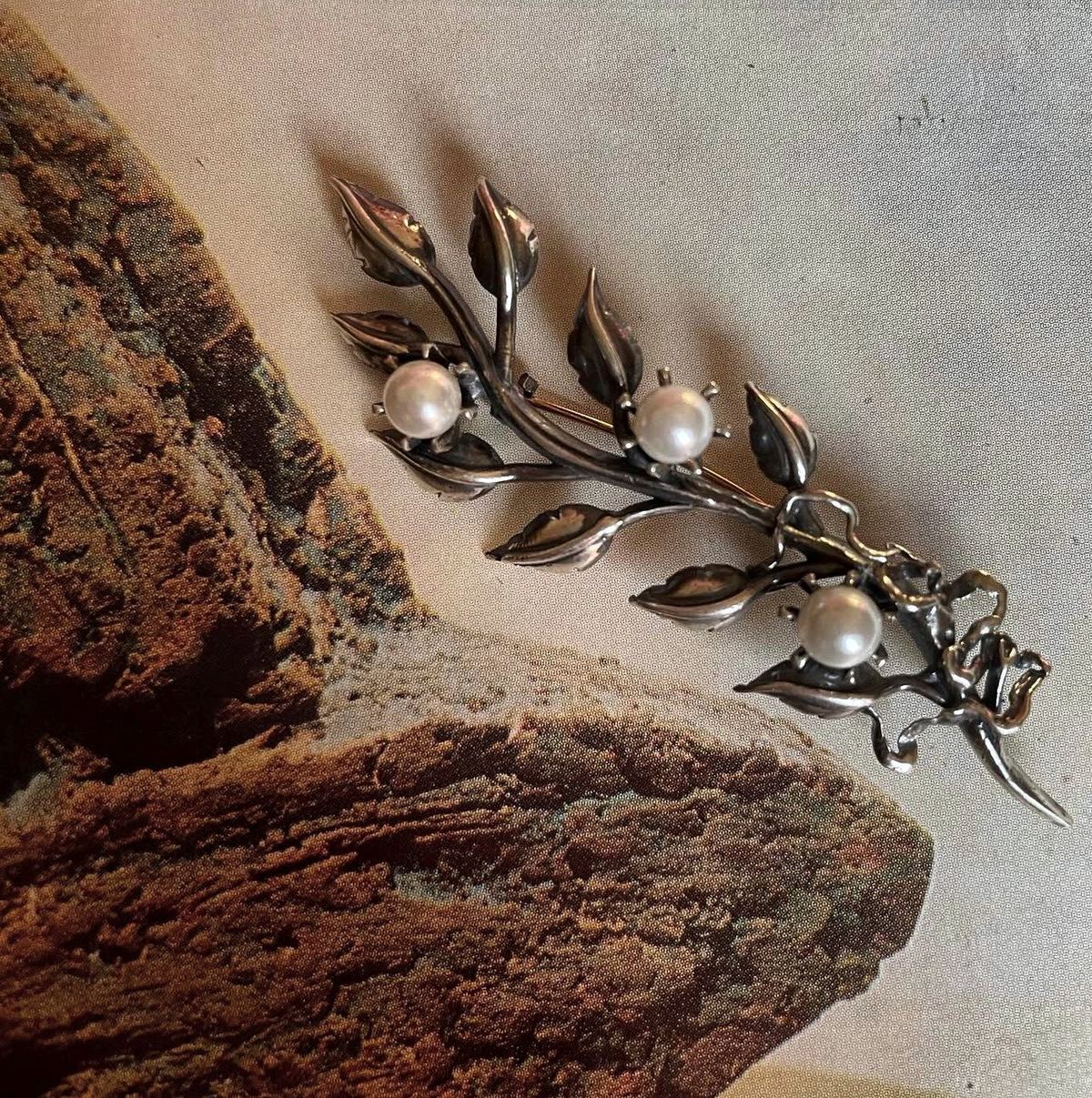 Broche de rama con hojas y perlas sobre una impresión de roca.