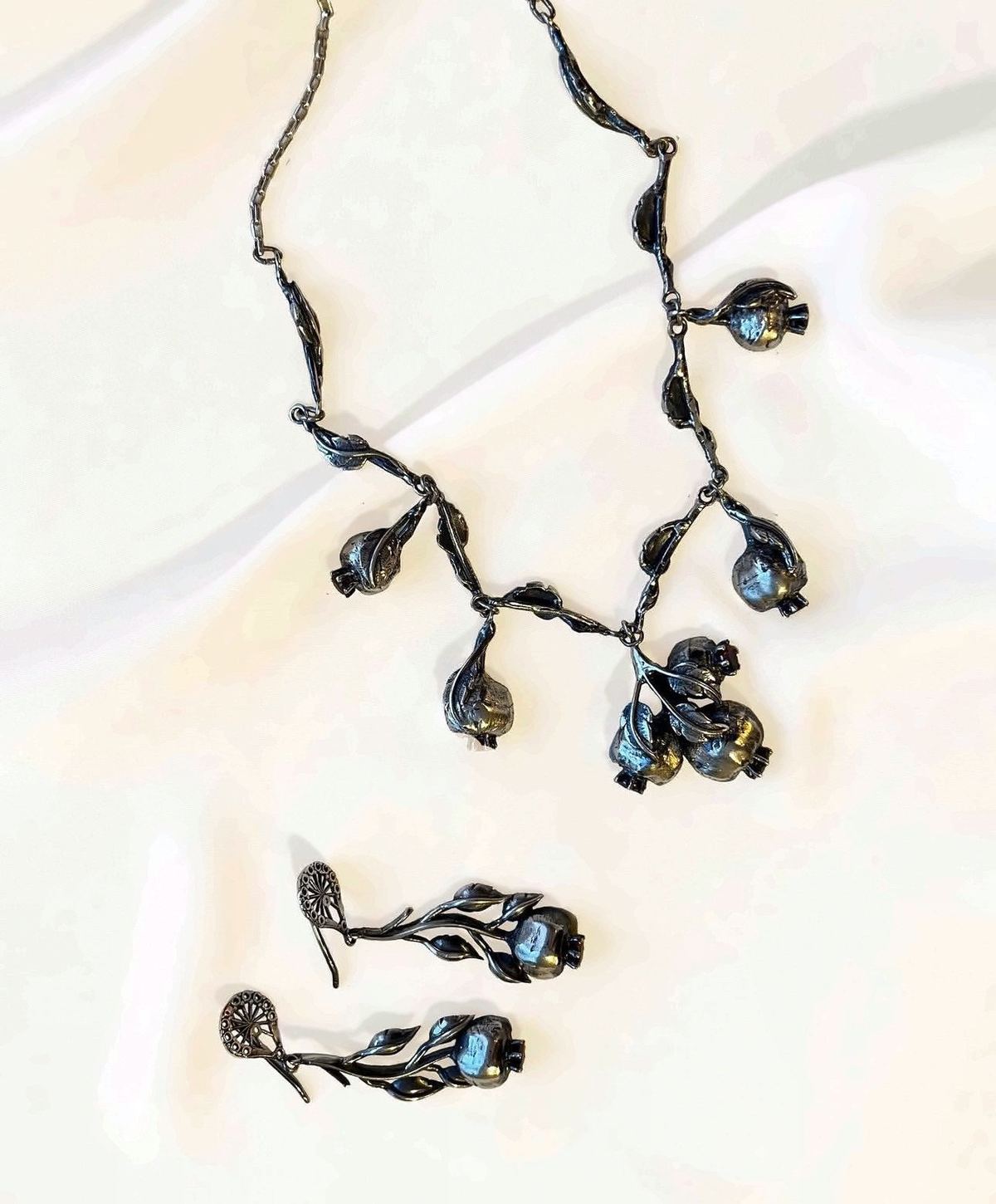 Silver necklace and earrings with pomegranate buds on cream cloth.