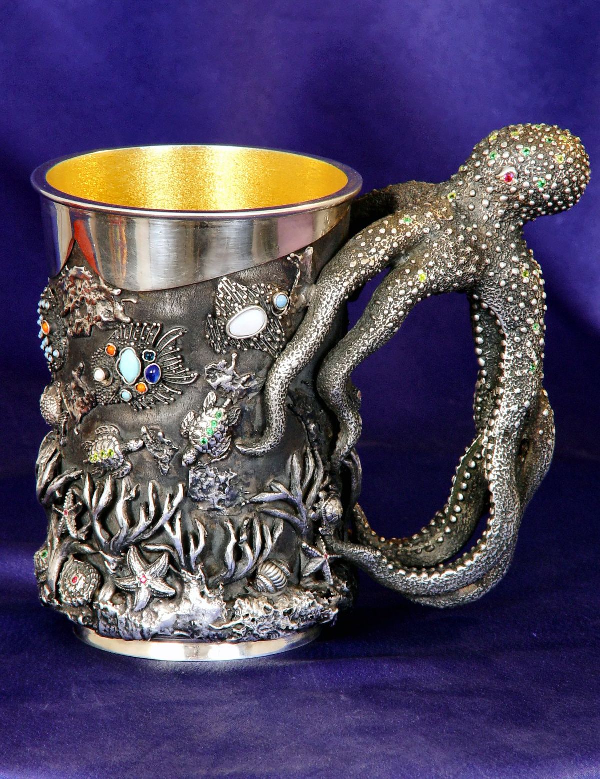 Silver tankard with an octopus-shaped handle, on purple cloth.