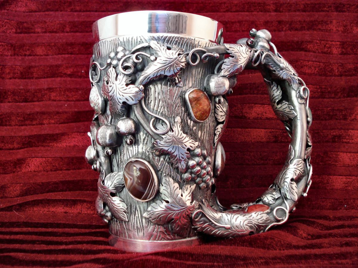 Silver tankard with vine relief and agates, on red velvet.