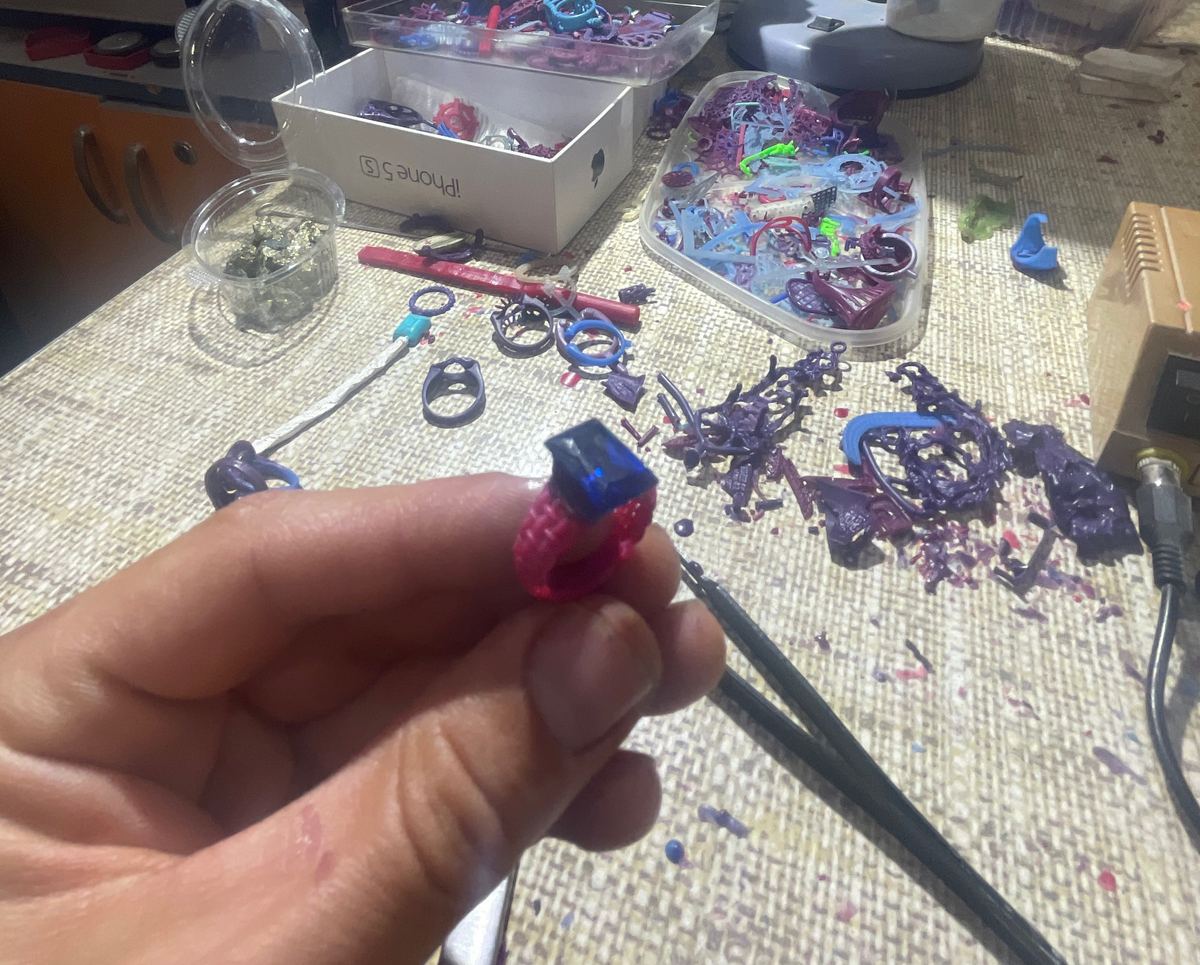 Wax model of a ring held in the hand over the workbench.